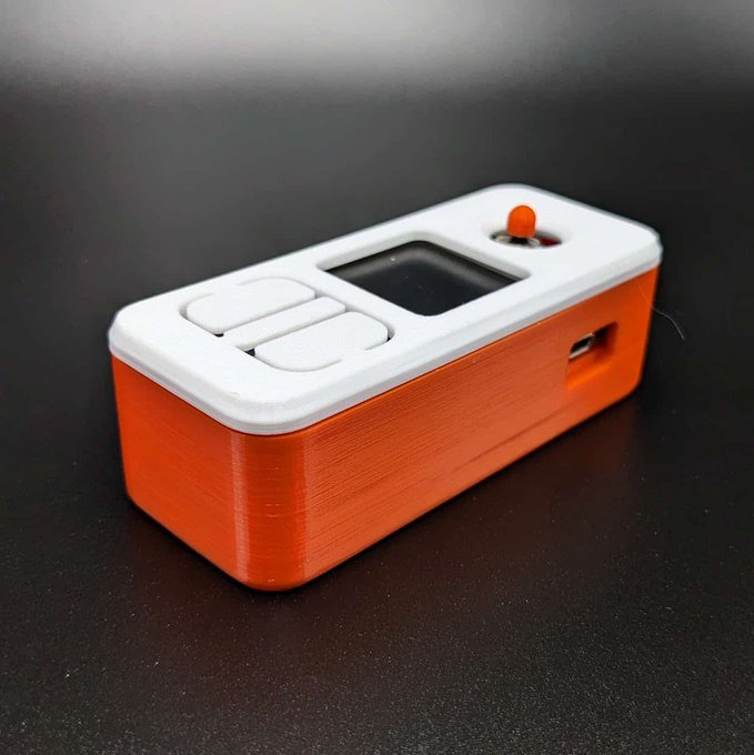 A SeedSigner hardware wallet sits in its orange 3D-printed "Orange Surf" protective case, featuring a small OLED screen, control buttons, joystick, and USB port. The image showcases the finished device that the accompanying post advertises as a $9.99 accessory printed in Colorado by cryptocloaks.com.