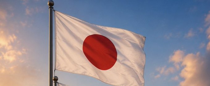 A photograph of the Japanese flag (white with a red circle) waving on a flagpole against a blue sky with scattered clouds at sunset.