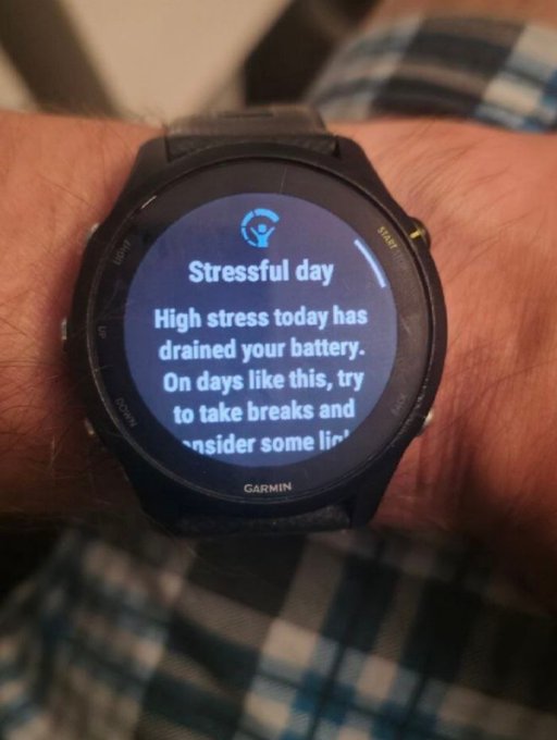 A Garmin smartwatch on a person's wrist displays a "Stressful day" notification, advising that high stress has drained the battery and suggesting breaks and lifestyle considerations.