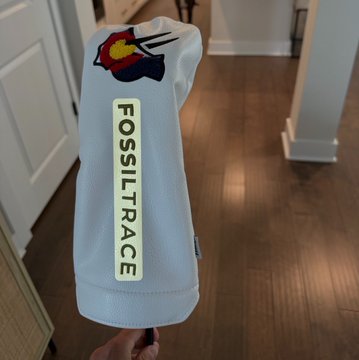 A light blue Fossil Trace sweatshirt is held up on display, featuring the brand's colorful flame logo and a vertical "FOSSILTRACE" name tag, connecting to the poster's mention of Fossil Trace as their favorite Colorado golf course.