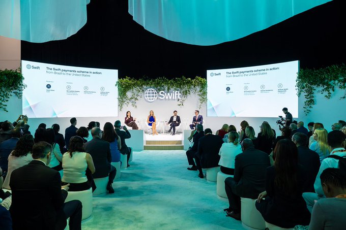 A panel discussion at a Swift event titled 'The Swift payments scheme in action: from Brazil to the United States,' featuring four speakers on stage with an audience seated in front of two large presentation screens.
