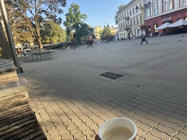 A coffee break captures a peaceful afternoon scene at what appears to be a European city square, possibly in Kyiv given the "KONTINENT" signage visible on a building in the background, with a person casually walking across the plaza. The relaxed café moment complements the "Good Afternoon CT" greeting in the post, suggesting a leisurely workday pause with mentions of Axis Robotics and DAC Chain.