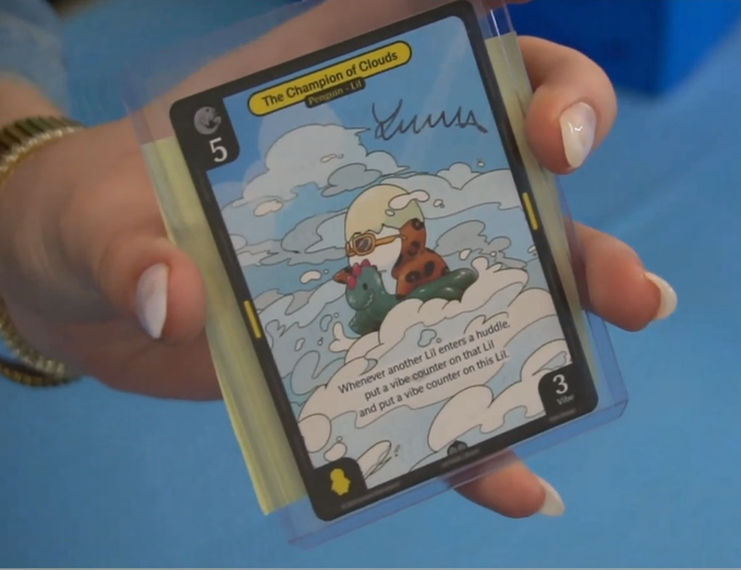 A hand holds a Pokemon trading card titled 'The Champion of Clouds' featuring an illustration of a figure on clouds. The card has a cost of 5, a value of 3, and text reading 'Whenever another Lil enters a hustle, put a vibe counter on that Lil and put a vibe counter on this Lil.'
