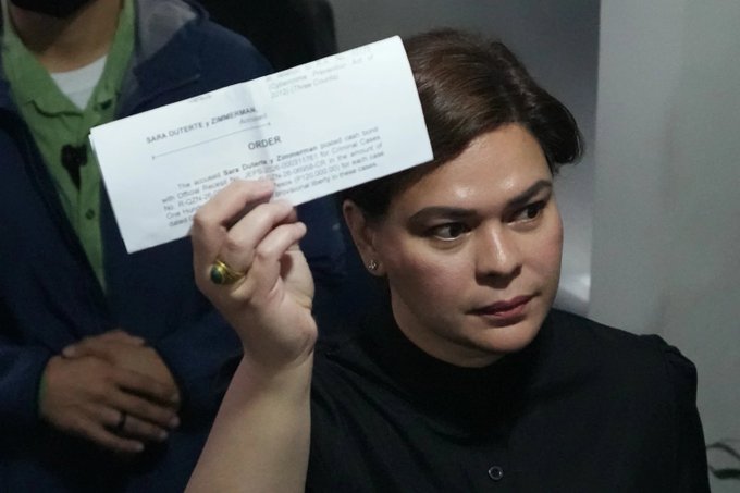 A young woman holding up a printed document labeled 'SARA DUTERTE v ZIMMERMAN' and 'ORDER', appearing to be a court document.