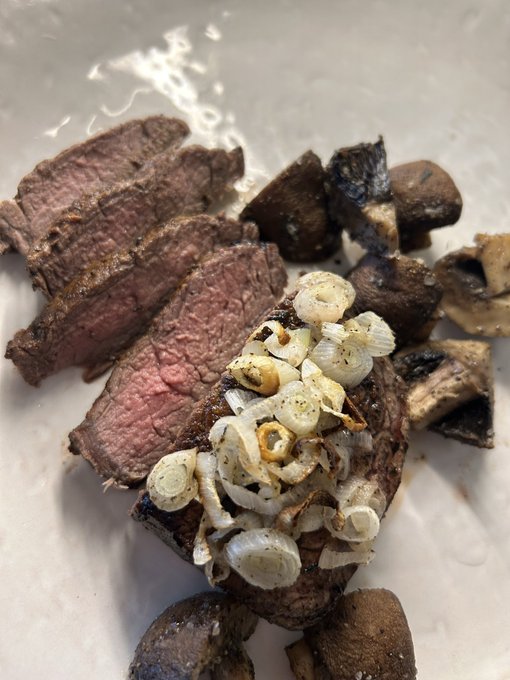 A plated dish features sliced medium-rare steak topped with caramelized onions, accompanied by sautéed mushrooms and potatoes.