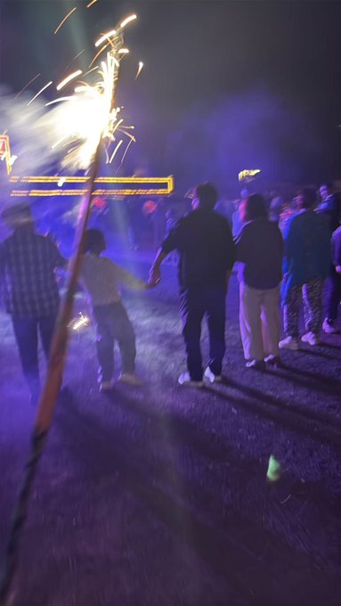 A group of people gathers at night around a crackling campfire with bright sparks shooting upward, set against a vivid blue-lit grassland backdrop, capturing a traditional Mongolian ceremony of prayer to the Eternal Blue Sky. The scene reflects the post's theme of participating in grassland customs to wish friends and readers prosperity and happiness.
