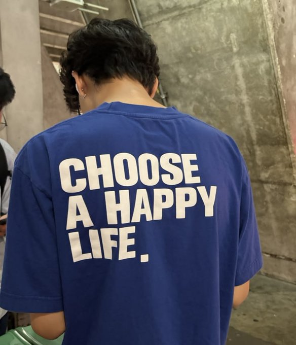A person viewed from behind wearing a blue t-shirt that reads 'CHOOSE A HAPPY LIFE.' in bold white letters.