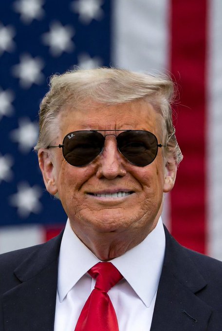 An older man with blonde hair, wearing aviator sunglasses, a dark suit, white shirt, and red tie, smiles broadly in front of an American flag. The caption humorously likens him to a "boss" announcing a $5,000 distribution to citizens, which the poster jokes will cause Bitcoin to soar—pairing the man's confident, commanding smile with the bold financial claim.