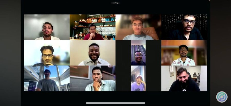 A Zoom video call with a 3x4 grid of twelve participants, showing 10 attendees visible on camera with one indicating '1 is talking' at the top.