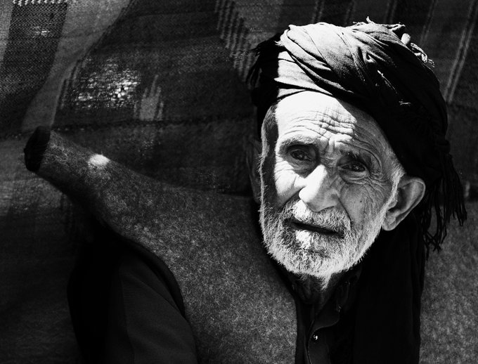 A black-and-white portrait of a weathered elderly man wearing a traditional turban, his face deeply lined and gazing directly at the camera. The image is presented as a 1/1 NFT artwork titled "Kurdish man," minted on the Tezos blockchain via objkt.com.