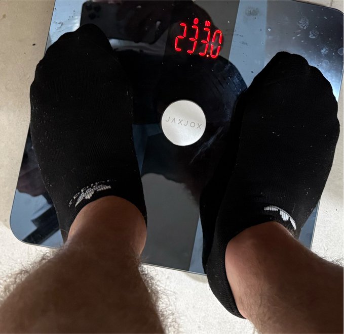 A person's sock-clad feet stand on a JAXJOX scale displaying a weight of 233.0, tracking progress toward a 300-pound weight goal as part of their #RoadTo300 fitness journey.