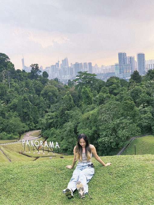 A young woman sits on a grassy hill overlooking a city skyline, with the text "PANORAMA" overlaid on the image.