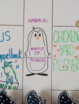 A drawing on white tiles featuring a penguin labeled 'WADDLE OF PENGUINS' under 'AMBER ALE', alongside other sketches including 'CHICKEN YARD PILSNER' and a blue character playing trumpet under 'APPELBOCK'.