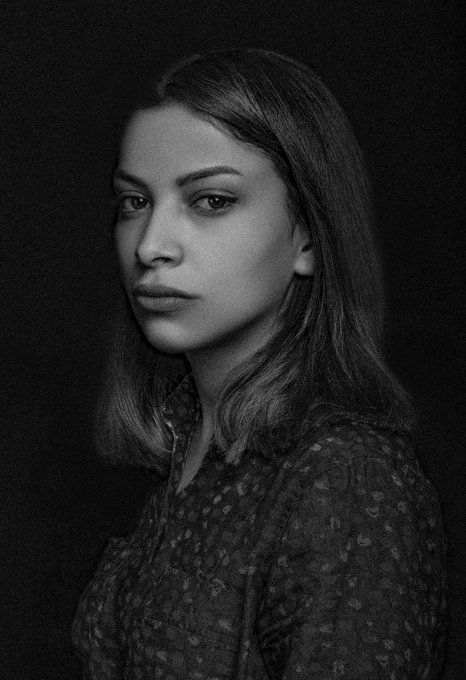 A black and white portrait of a woman with long hair, wearing a floral patterned blouse, gazing directly at the camera against a dark background. The contemplative, artistic image fits the aesthetic of the Tezos NFT community post celebrating #TEZOSTUESDAY, likely serving as the artwork for the featured NFT token.
