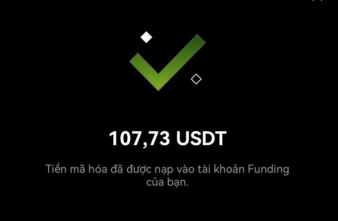 A dark screen with a green checkmark displaying '107,73 USDT' and Vietnamese text confirming 'Tiền mã hóa đã được nạp vào tài khoản Funding của bạn' (Cryptocurrency has been deposited into your Funding account).