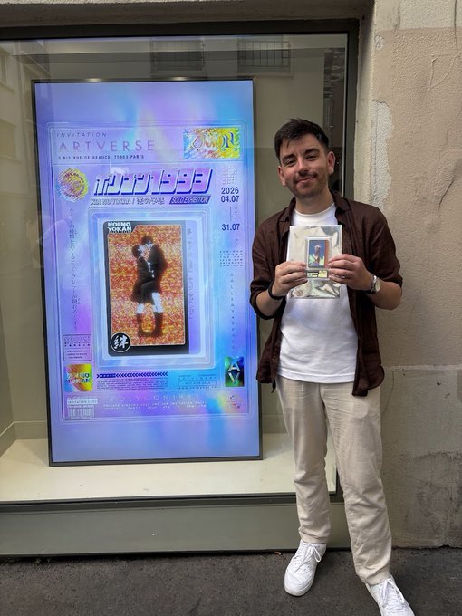 A man in a brown shirt, white t-shirt, and beige pants holding a small framed item while standing next to a poster for an "ARTVERSE" exhibition at Paris City Hall, with Korean text "인사동" and dates "2026.04.07 – 31.07".