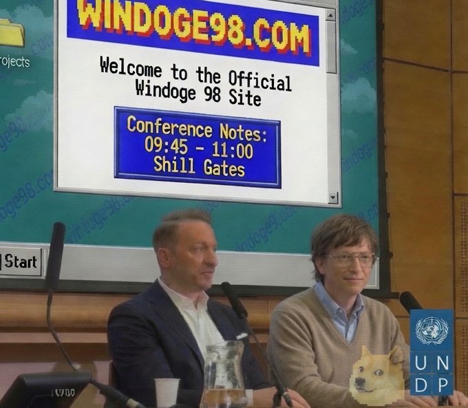 Two men sit at a conference panel in front of a screen displaying "WINDOGE98.COM - Welcome to the Official Windoge 98 Site" with "Conference Notes: 09:45 - 11:00 Shill Gates," referencing Bill Gates in a meme mocking the ICP cryptocurrency project.

The image ties to the post as a humorous jab at ICP's ambitious "World Computer" vision, with the parody Windows 98-styled site ("Windoge" being a crypto doge meme) satirizing how the project tries to position itself as a global operating system by featuring a "Shill Gates" speaking slot.