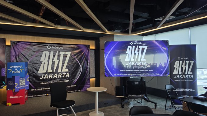 A conference room setup featuring large 'BLITZ JAKARTA' banners for a Monad blockchain event, with branded displays for 'Connet' guild and 'BlockDev'.