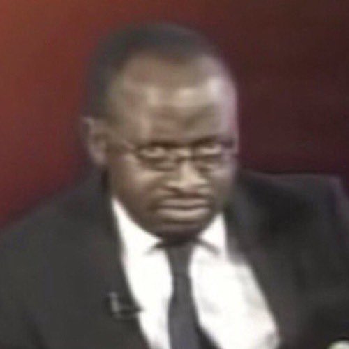 A grainy image shows a man in a suit and tie looking downward with a serious expression.