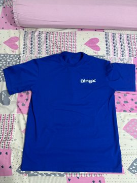 A blue t-shirt with the text 'bingx' printed in white on the chest, laid out on a pink and white patterned bed sheet.