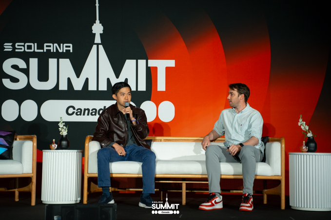 Two men seated on a stage at the SOLANA SUMMIT Canada event, with one speaking into a microphone while wearing a brown leather jacket.