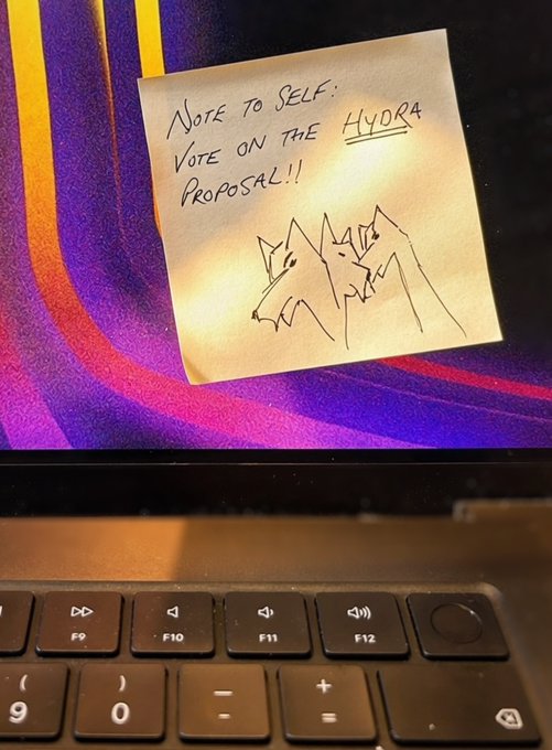 A yellow sticky note on a laptop screen reads "Note to Self: Vote on the Hydra Proposal!!" alongside a hand-drawn sketch of a multi-headed hydra creature, serving as a visual reminder to cast a vote on the Hydra governance proposal before it closes.