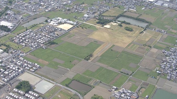 An aerial view shows agricultural fields, residential areas, and rural infrastructure typical of a Japanese suburban landscape, possibly near an airport given the long rectangular clearing. The celebratory post about a "Sui envoy" appears unrelated to the image content, with no visible text, numbers, or identifiable landmarks connecting to the congratulatory message.