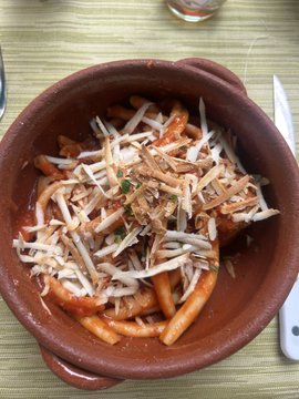 xtremely delicious pasta dish with red sauce, white noodles, and brown cheese crumbles is served in a rustic clay pot on a green tablecloth.