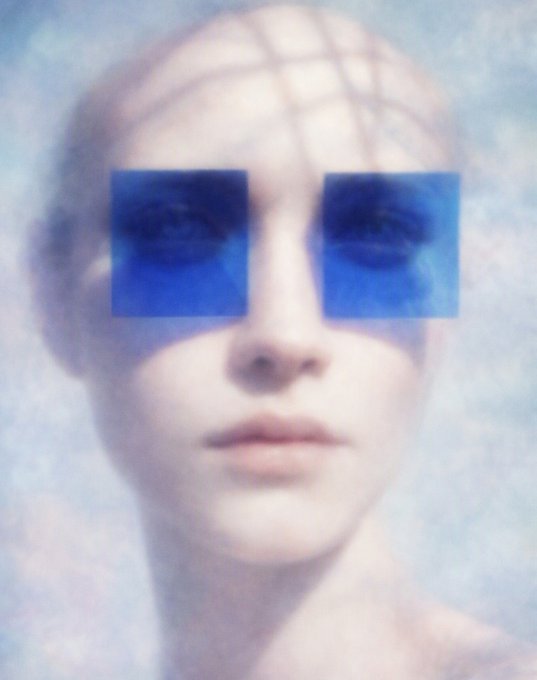 A pale sculptural bust of a face with a grid pattern projected across the forehead and two blue square overlays covering the eye areas, giving it a surreal, digital aesthetic.