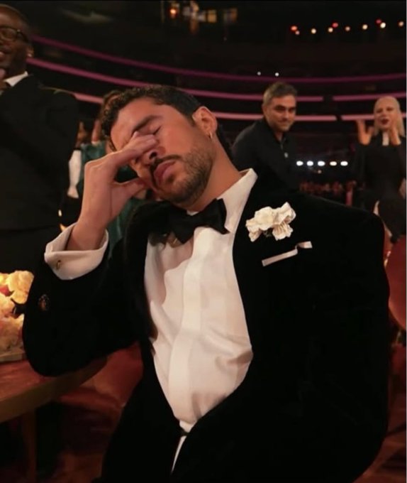 The image shows a man in a tuxedo with a white boutonnière, pinching the bridge of his nose with his eyes closed in apparent frustration or exasperation, seated at what appears to be a formal awards ceremony. The accompanying post humorously compares the man's expression to Jim Cramer's reaction upon witnessing Bitcoin's price surge shortly after selling his holdings, suggesting the universal feeling of regret when missing out on a major crypto rally.