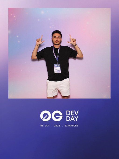 A man wearing a black shirt and white shorts poses with both index fingers pointing up at the 0G Dev Day event on October 5, 2026, in Singapore.