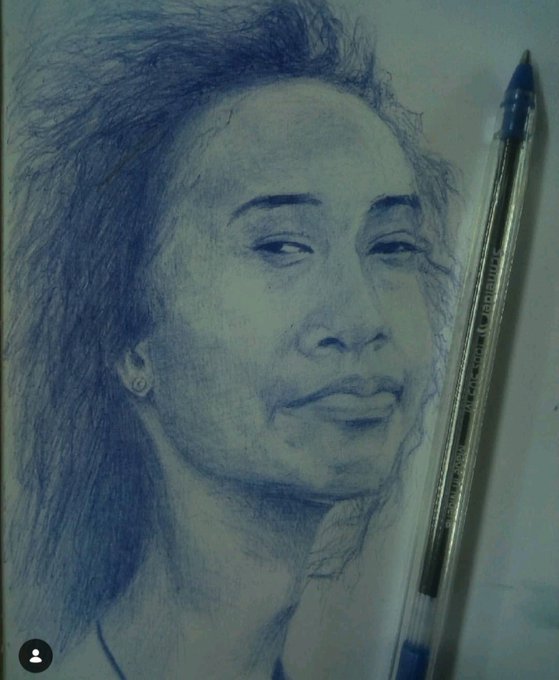 A pencil sketch portrait of a woman with dark hair and an earring, drawn in blue tones on light paper, with a blue ballpoint pen placed diagonally next to the drawing.