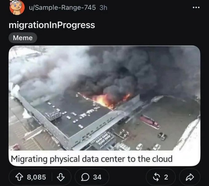 A Reddit meme posted by u/Sample-Range-745 showing an aerial view of a burning building with thick black smoke, captioned 'Migrating physical data center to the cloud,' with 8,085 upvotes.