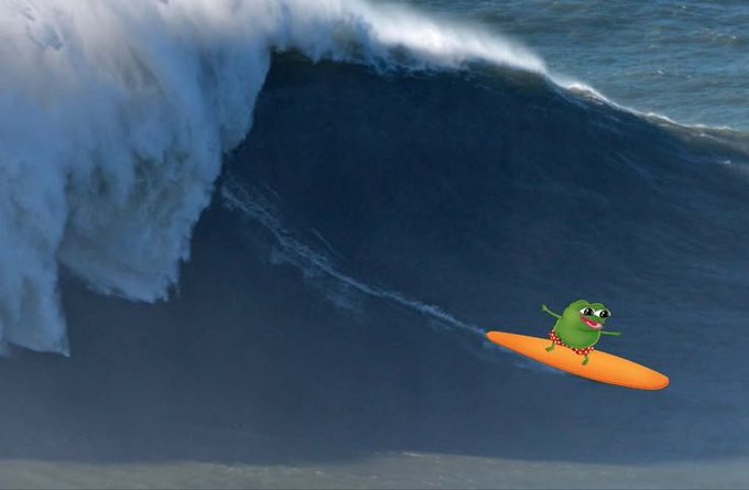 A cartoon green frog character rides an orange surfboard down the face of a massive, towering wave, with the frog's playful expression and the enormous scale of the wave creating a humorous "good morning" greeting that suggests taking on a big day with a smile.