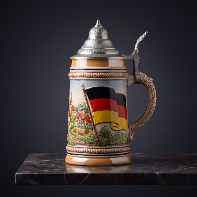The image features a mug that has a German flag painted on it, sitting on top of a marble countertop or table. The mug is adorned with an illustration of a village scene, which includes houses and trees. The mug also has a handle on one side for easy carrying. The background of the image is black, making the colorful mug stand out prominently. The post that accompanies this image reads: "GM ! Watching the worldcup with an @opensea nft made by @ExoticRaccoon hits different. Let'S go Germany". This message seems to be related to a recent soccer match or event involving the German flag, possibly celebrating their national team's victory in the World Cup.