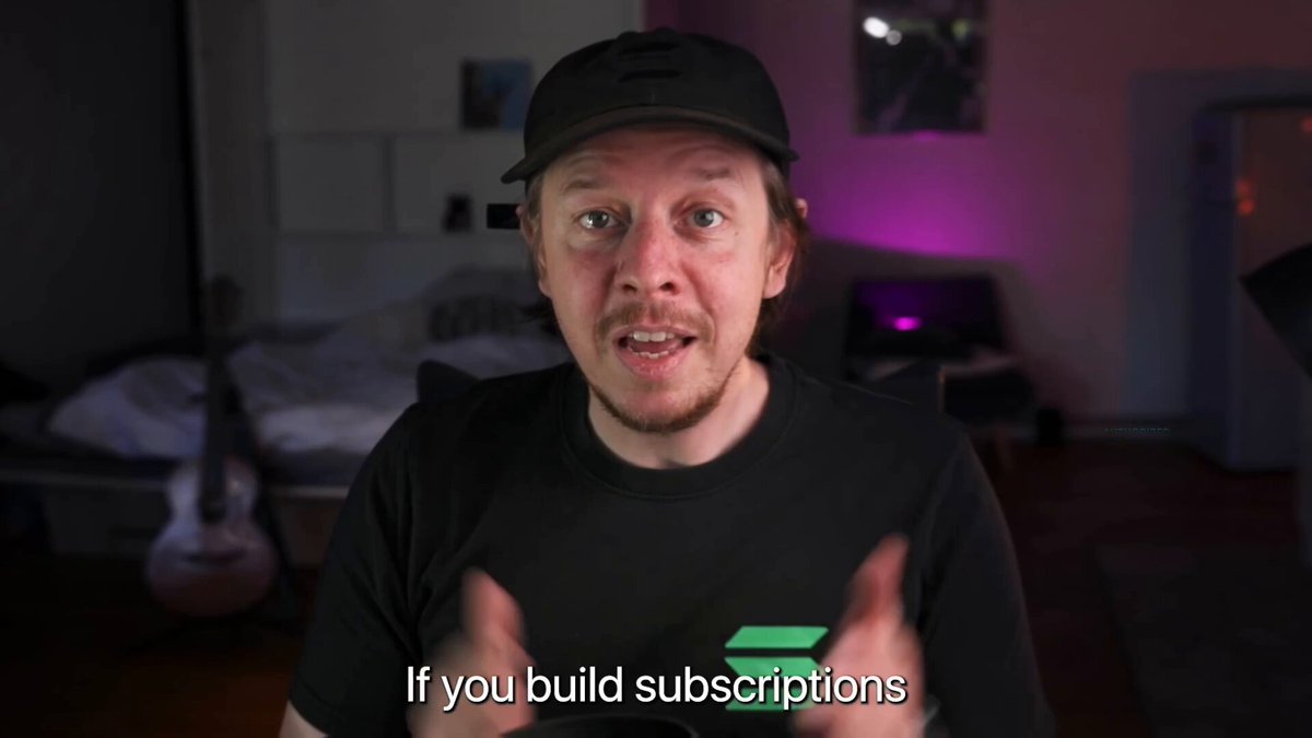 The image shows a man wearing a black baseball cap, sitting at a desk with his hands outstretched as if he's giving instructions or explaining something. The background of the image features a bed and a guitar, suggesting that this scene takes place in a bedroom setting. There is also text on the image that reads "If you build subscriptions", which could be related to the content being discussed by the man at the desk.