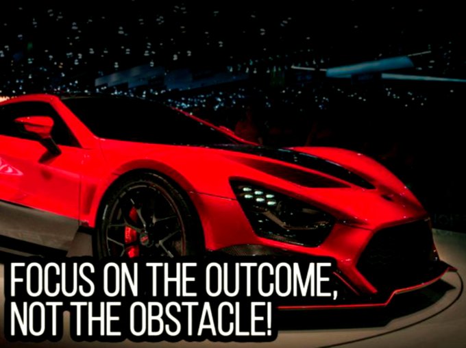 A red sports car is displayed on stage with bold text reading 'FOCUS ON THE OUTCOME, NOT THE OBSTACLE!'
