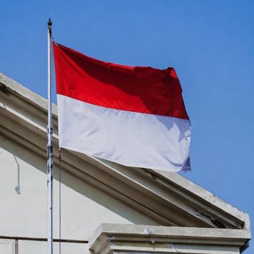 The image features a red and white flag flying high above a building with a white roof. The flag has the colors red and white, which are the national colors of Indonesia. Below the flag, there's an advertisement for a betting site called @Polymarket that is currently banned in Indonesia due to concerns about gambling addiction among its users. This post also discusses the future of polymarket and the negative impact it could have on society.