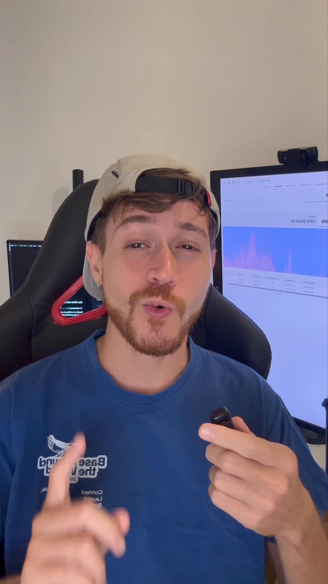 In this image, there's an adult male wearing a blue shirt sitting in front of his computer monitor with his arms up in the air. He appears to be giving instructions or explanations through a video call. The text "@base" can be interpreted as either being part of the caption or possibly something about the internet connection. A microphone is also present near him, indicating that he might be recording his voice for the video call. On the monitor behind him, there's some data displayed which could potentially be related to what he is saying in the image. The post features an interesting combination of visual elements like a graphic and text with the man speaking into a microphone during a video call.