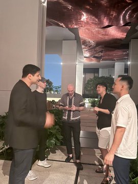 A group of men standing and talking in what appears to be a hotel lobby or similar modern indoor space with a decorative ceiling.