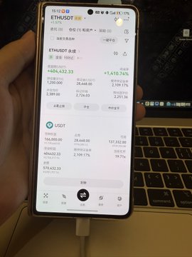 A hand holds a smartphone displaying a cryptocurrency tracking app with prices for 'ETH/USDT' (+1,432.33) and 'USDT' shown against a laptop keyboard.