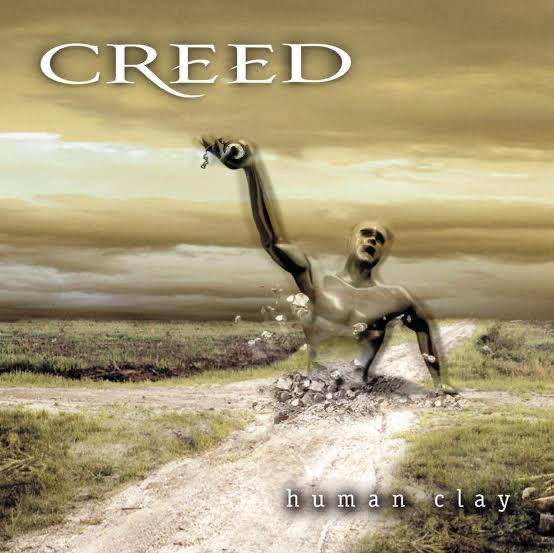 Album cover for 'Creed - Human Clay' showing a humanoid clay figure emerging from the ground along a dirt path under a cloudy sky.