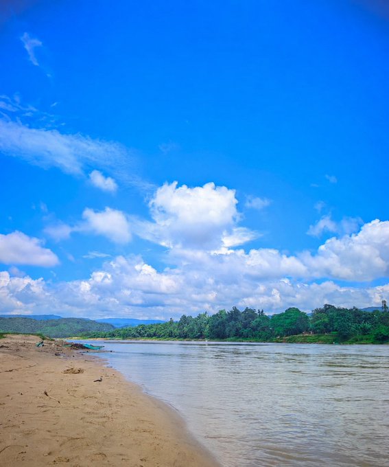 A serene sandy beach meets calm waters under a vibrant blue sky filled with fluffy white clouds, with lush green hills in the distance. The peaceful, open landscape mirrors the post's message of steady, focused work—suggesting that just as nature rewards consistent effort, so does staying active in Web3 lead to new opportunities.