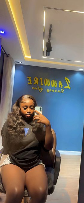 A woman with long wavy hair takes a mirror selfie with her phone in a salon called 'RAWIRE Hair & Glamour Salon'.