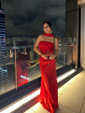 A woman in an elegant red evening gown poses with a wine glass on a high-rise balcony overlooking Hong Kong's illuminated skyline at night, with a partially visible "BANK OF [America]" sign below—setting a sophisticated scene fitting the @Bitcoinconfasia conference atmosphere.