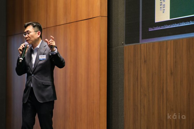 A man in a dark suit speaks into a microphone while gesturing, delivering a keynote address beside a presentation screen displaying what appears to be a slide with Asian characters. The image aligns with the post, capturing KaiaChain Chairman Seo Sangmin delivering his Title Sponsor keynote at Blockfesta's onchain session on stablecoin issuance.
