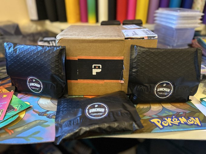 A cardboard box with a black 'P' logo on tape is flanked by three black bubble mailers bearing 'Frensly' branded stickers, arranged on a Pokemon playmat.