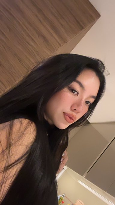 A selfie of a young woman with long dark hair indoors.