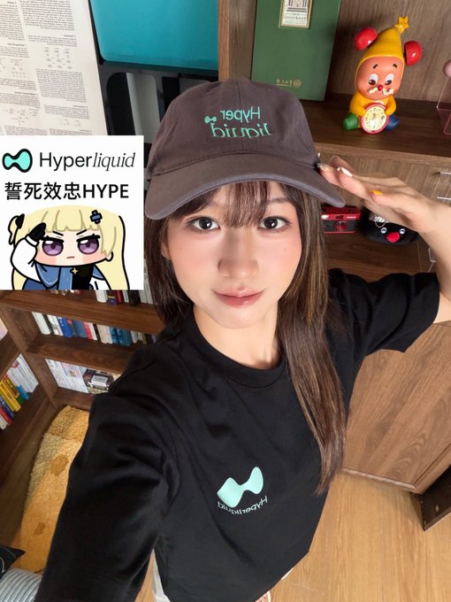 A young woman poses for a selfie while wearing a brown "Hyperliquid" cap and a black t-shirt featuring the teal Hyperliquid logo, matching the promotional text overlay reading "Hyperliquid 誓死效忠HYPE" alongside an anime character illustration. The cozy background—complete with bookshelves, an Anpanman clock, and plush toys—gives a personal, casual vibe that complements the post's invitation for fans to share their crypto struggles and potentially win 9.99 $HYPE.