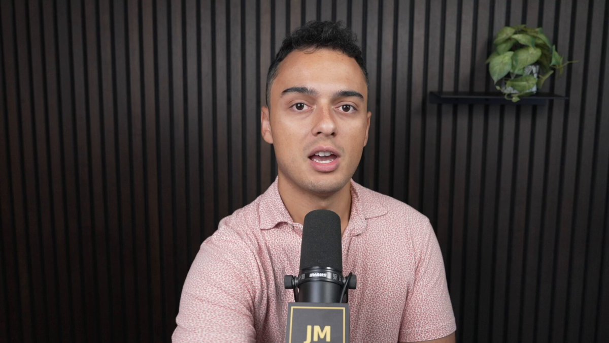 This is a microphone recording of an interview between a man wearing a pink shirt with white writing. There are some plants present near him which add a touch of nature to the indoor setting, possibly suggesting that this may be a studio session or an interview in someone's home environment. The focus on TAO and its timestamps indicates that the content is related to an Open AI podcast where they discuss various topics like AI, ethics, technology, and more.